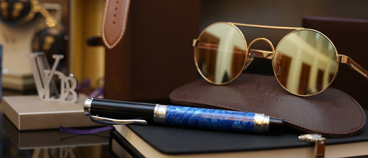 Luxury expensive pens with intricate design placed next to sunglasses and leather accessories